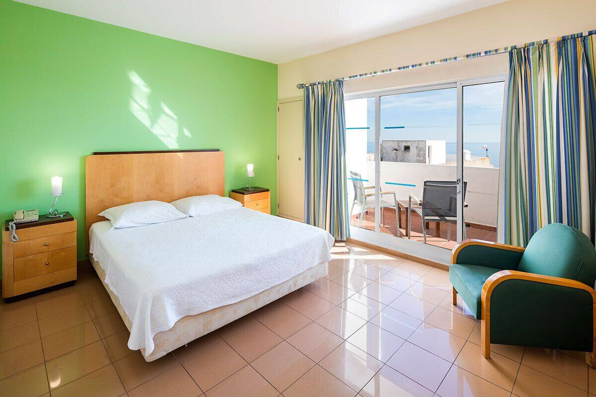 Habitació d'hotel amb un llit, una nit, una cadira i un balcó amb vistes.