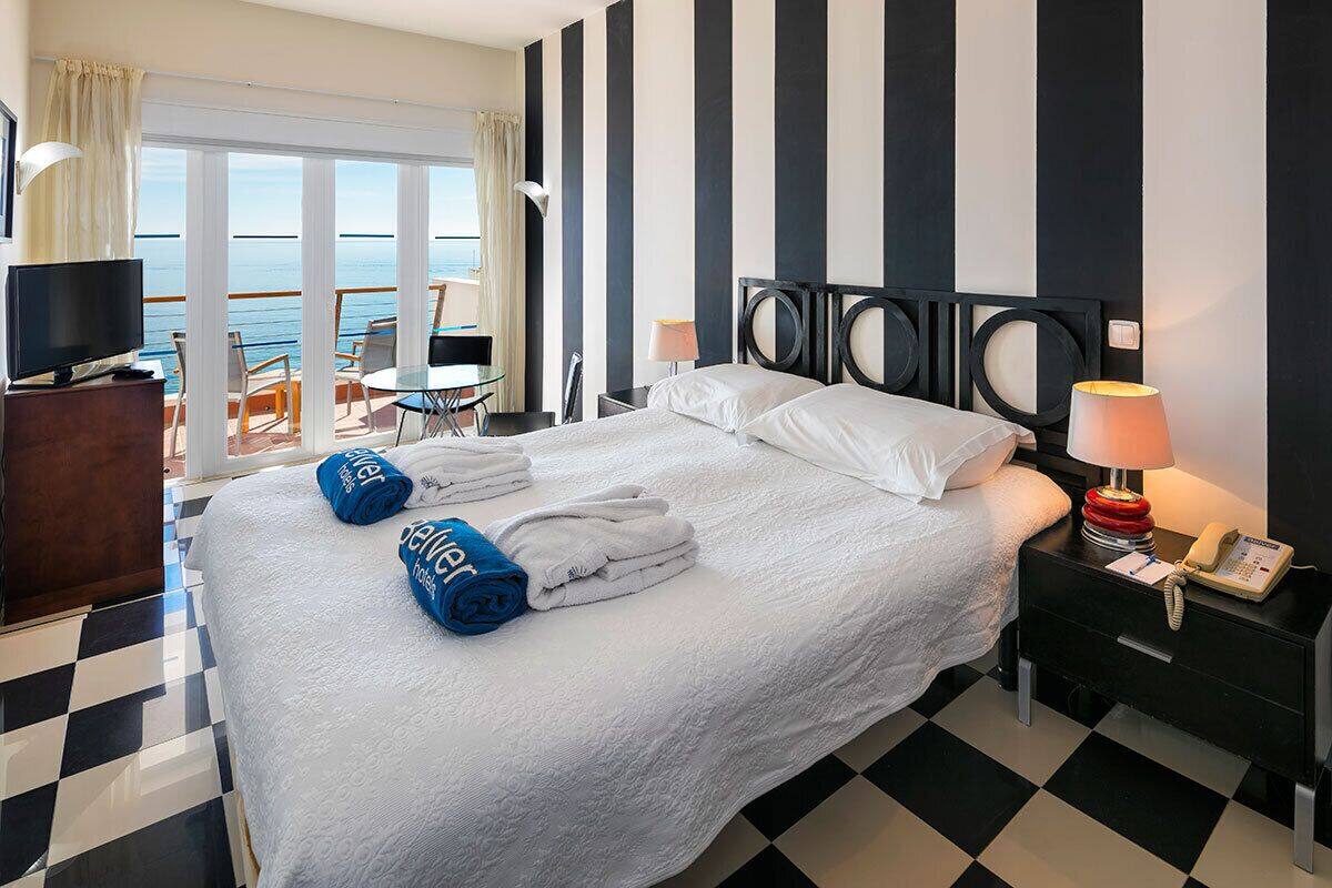 Una habitació d'hotel amb un llit, una televisió, un escriptori amb una làmpada i vistes al mar.