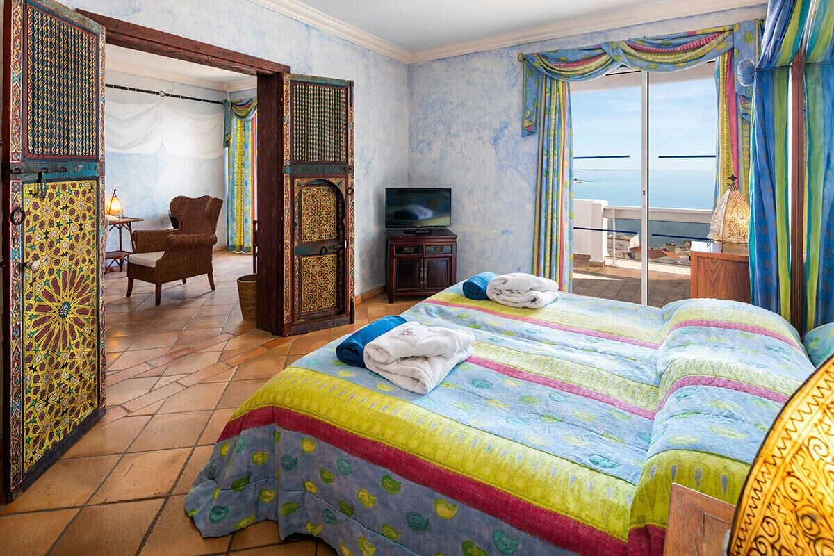 Een hotelkamer met een groot bed, een televisie, een stoel en uitzicht op zee.