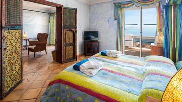 Een hotelkamer met een groot bed, een televisie, een stoel en uitzicht op zee.