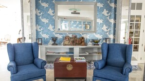 Una habitación con dos sillones azules, una mesa de centro de madera, un espejo decorativo y un papel tapiz estampado.