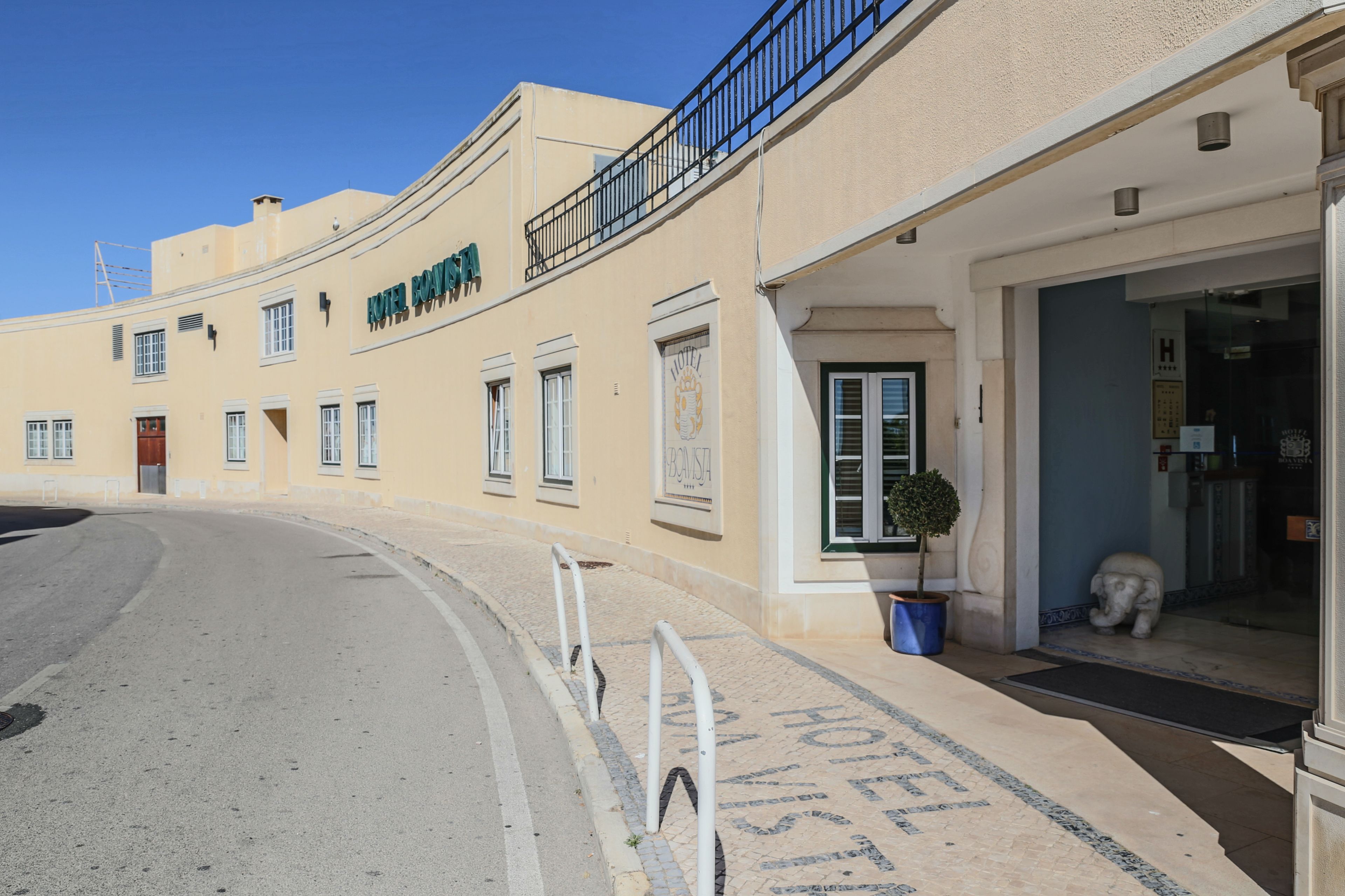 A hotel facade with a balcony, a potted plant, and a statue outside the entrance.