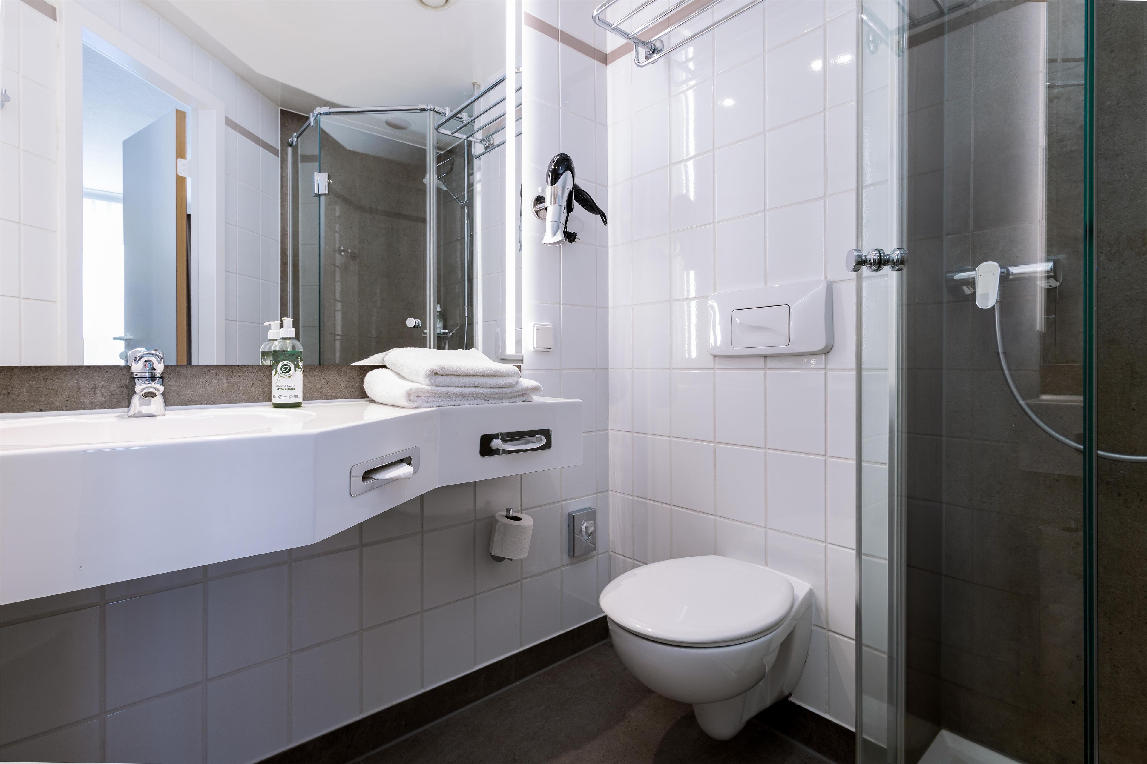 A modern bathroom with a glass shower enclosure, a white toilet, and a vanity with a mirror and towel rack.