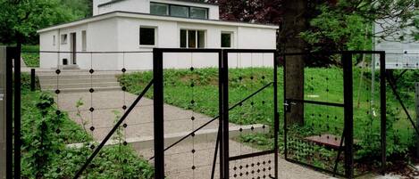 Un edificio moderno con fachada blanca, entrada protegida por una reja y una escalera que lleva a la entrada.