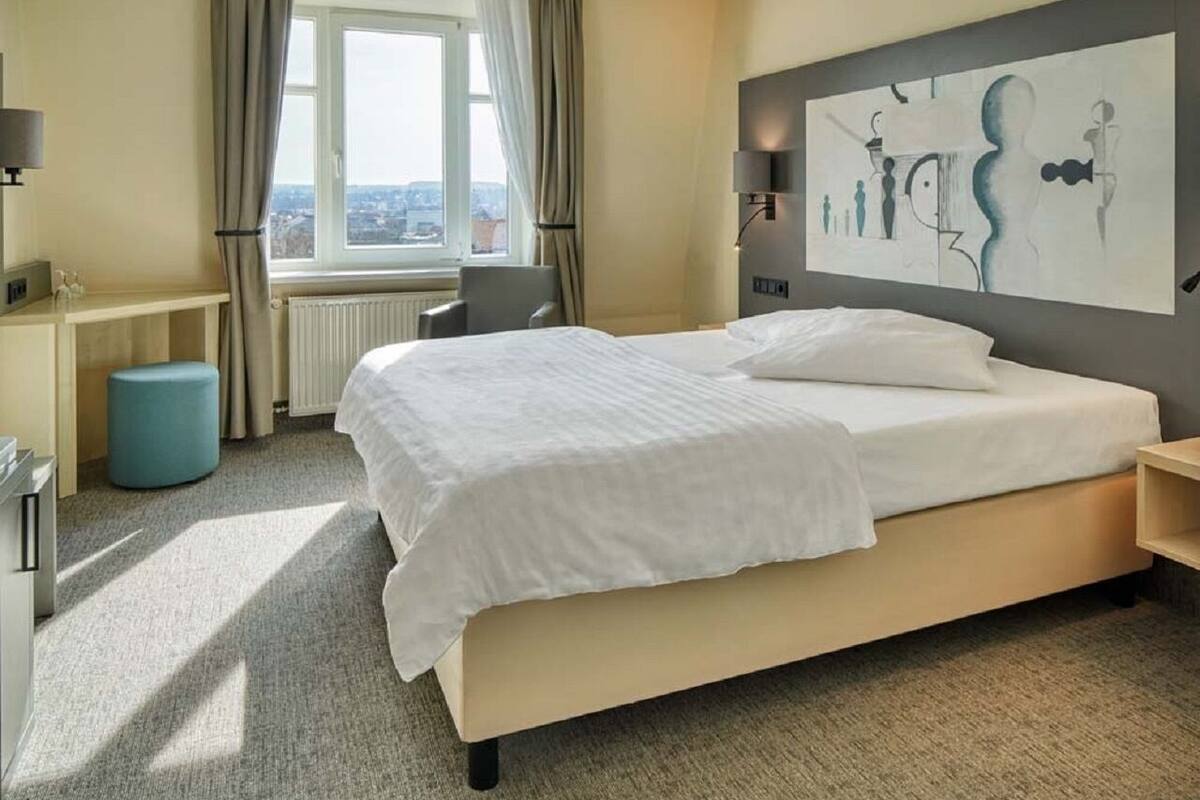 A hotel room with a large bed, a desk, a chair, and a window with curtains.
