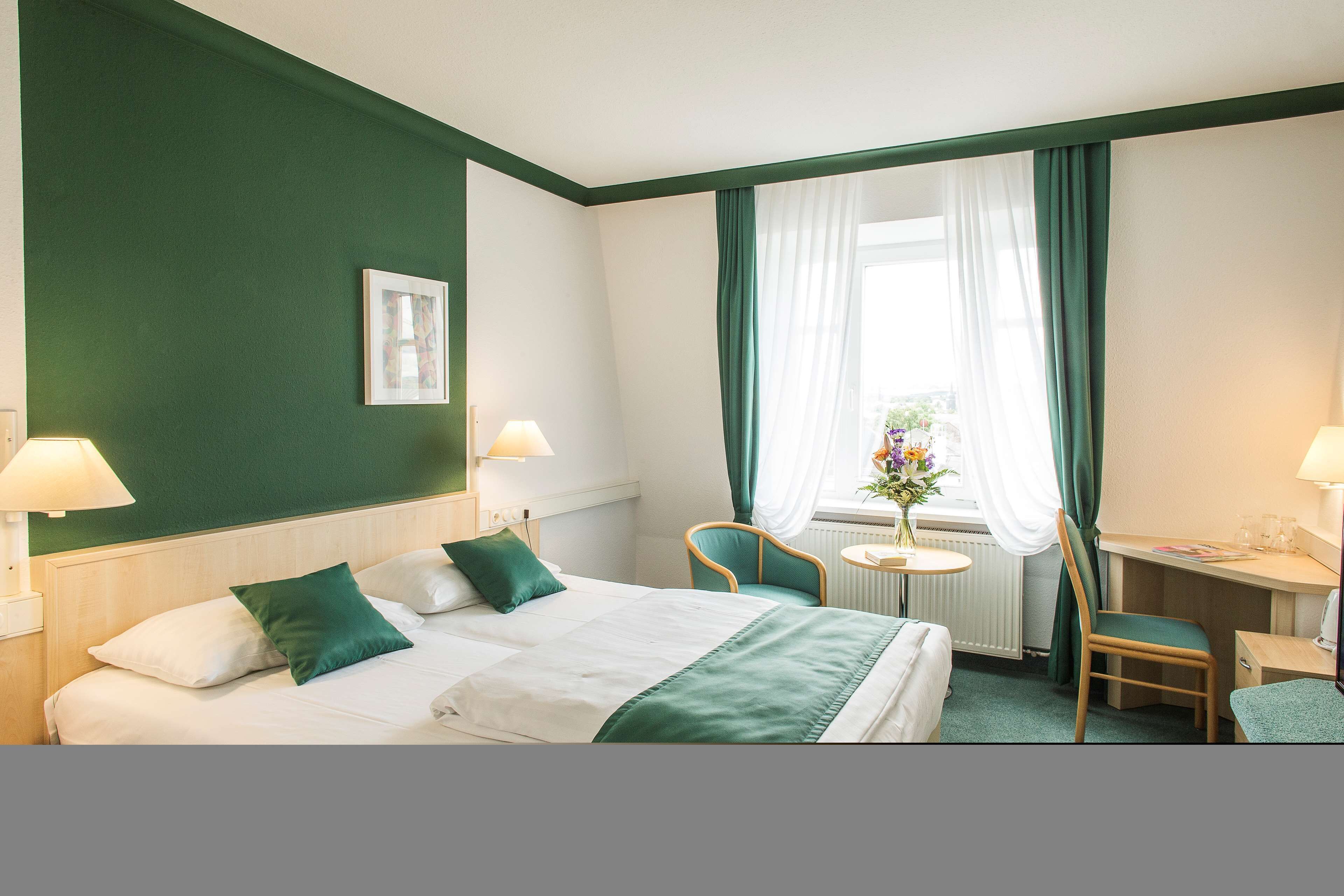 Ein Hotelzimmer mit Bett, zwei Stühlen, einem Schreibtisch und einem Fenster mit Vorhängen.