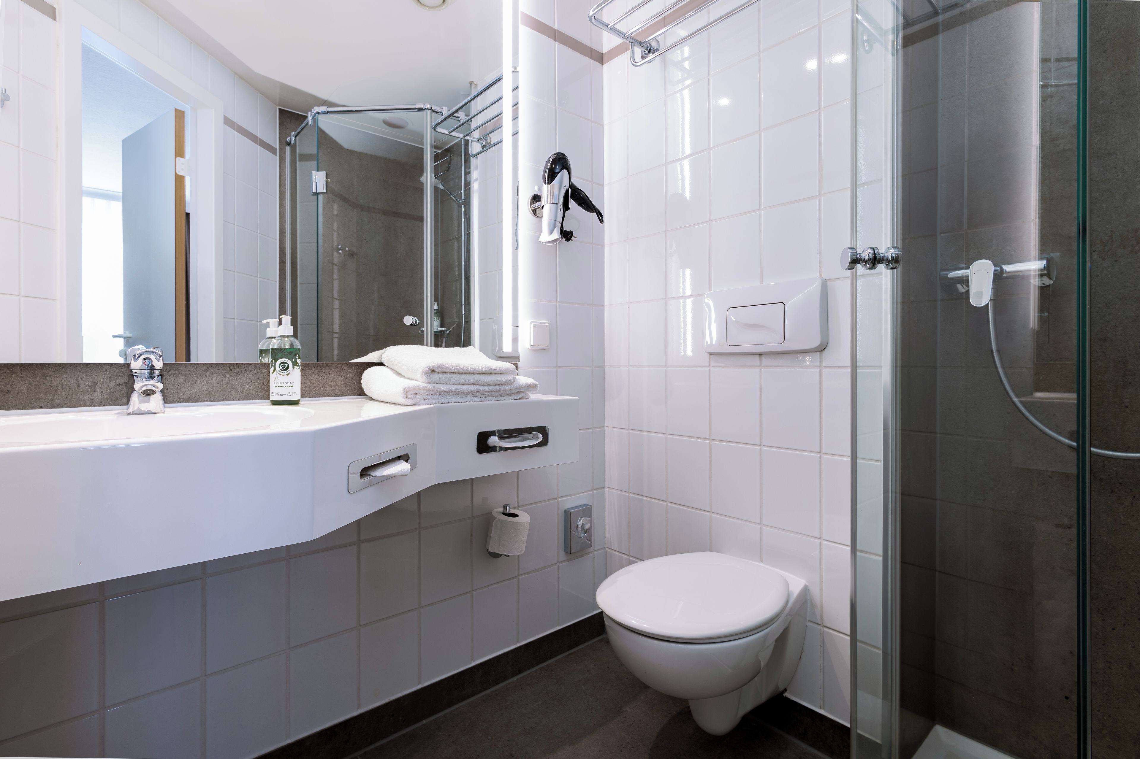 A modern bathroom with a white sink, mirror, and toilet.