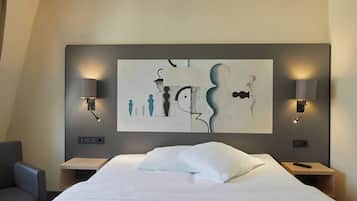 Ein Hotelzimmer mit einem großen Bett, zwei Nachttischen, einem Sessel und einem an der Wand befestigten abstrakten Kunstwerk.