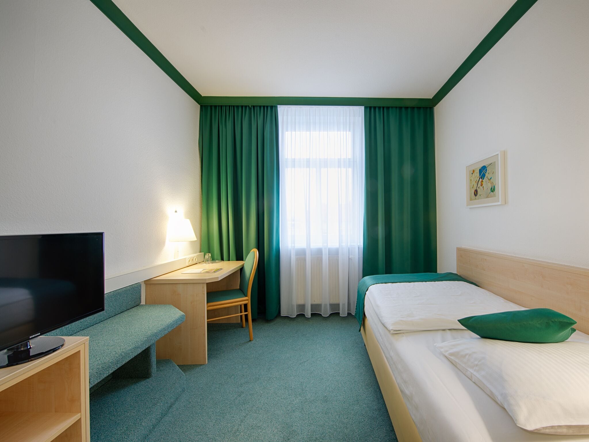 Habitación de hotel con cama, escritorio, silla, televisión y ventana con cortinas.