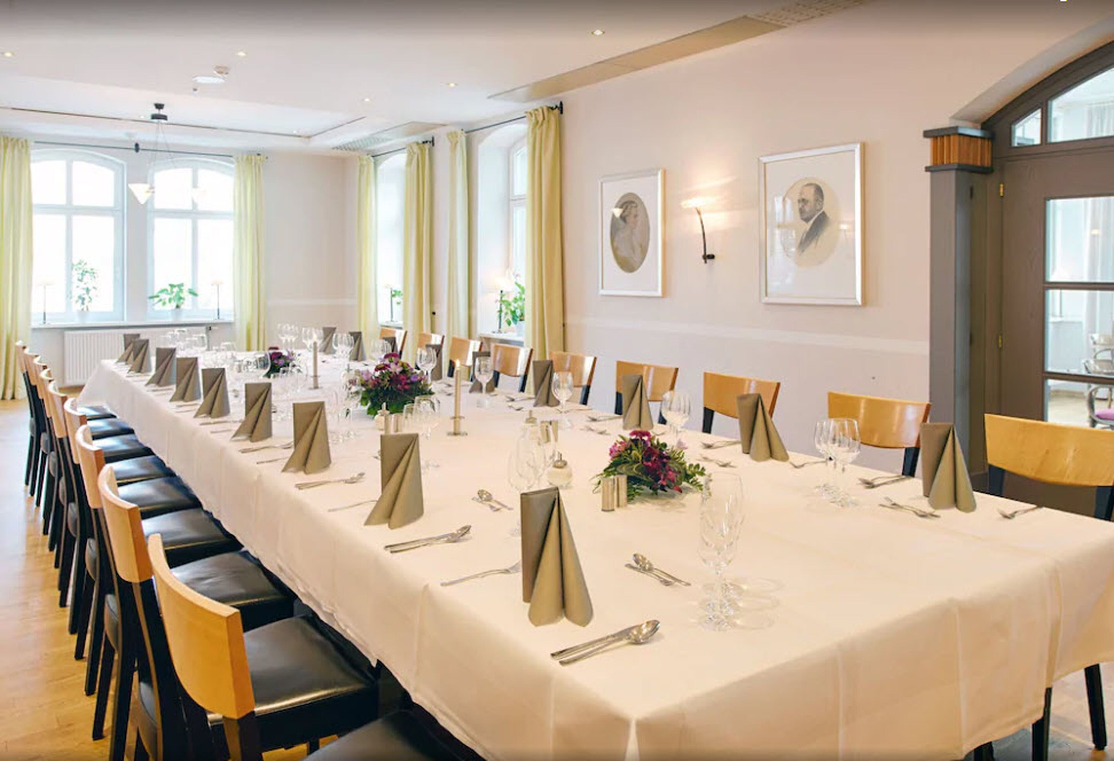 Una larga mesa de comedor dispuesta para un evento formal, con sillas, vajilla y cuadros en las paredes.