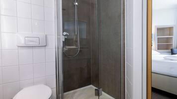 Un baño moderno con ducha envuelta en vidrio, inodoro y lavamanos blanco.