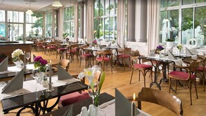 A spacious dining area with multiple tables and chairs, large windows with curtains, and a view of the outdoors. - Hotel Kaiserin Augusta (Weimar)