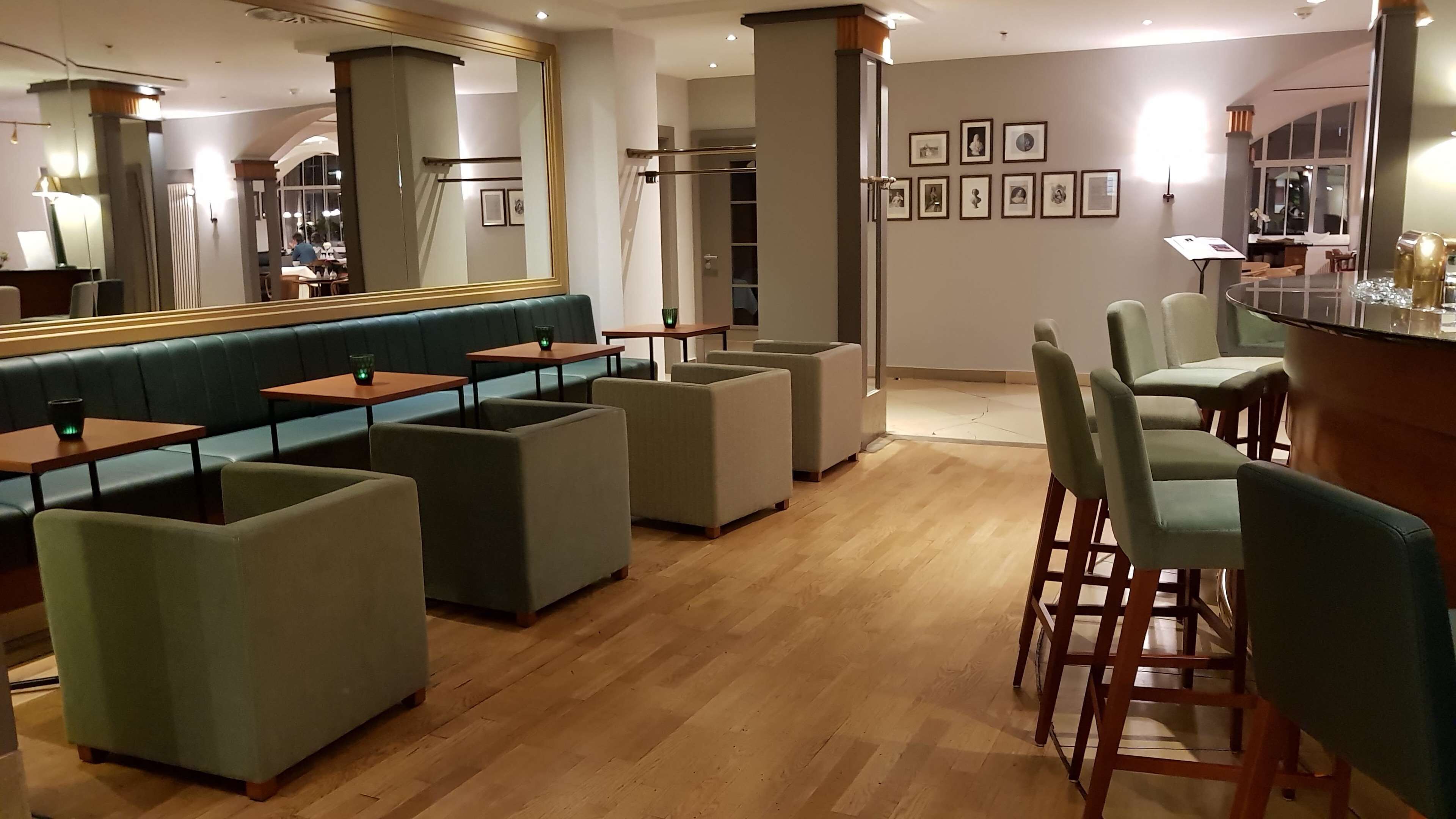 Un restaurante moderno con suelo de madera, asientos acolchados verdes y una zona de bar.