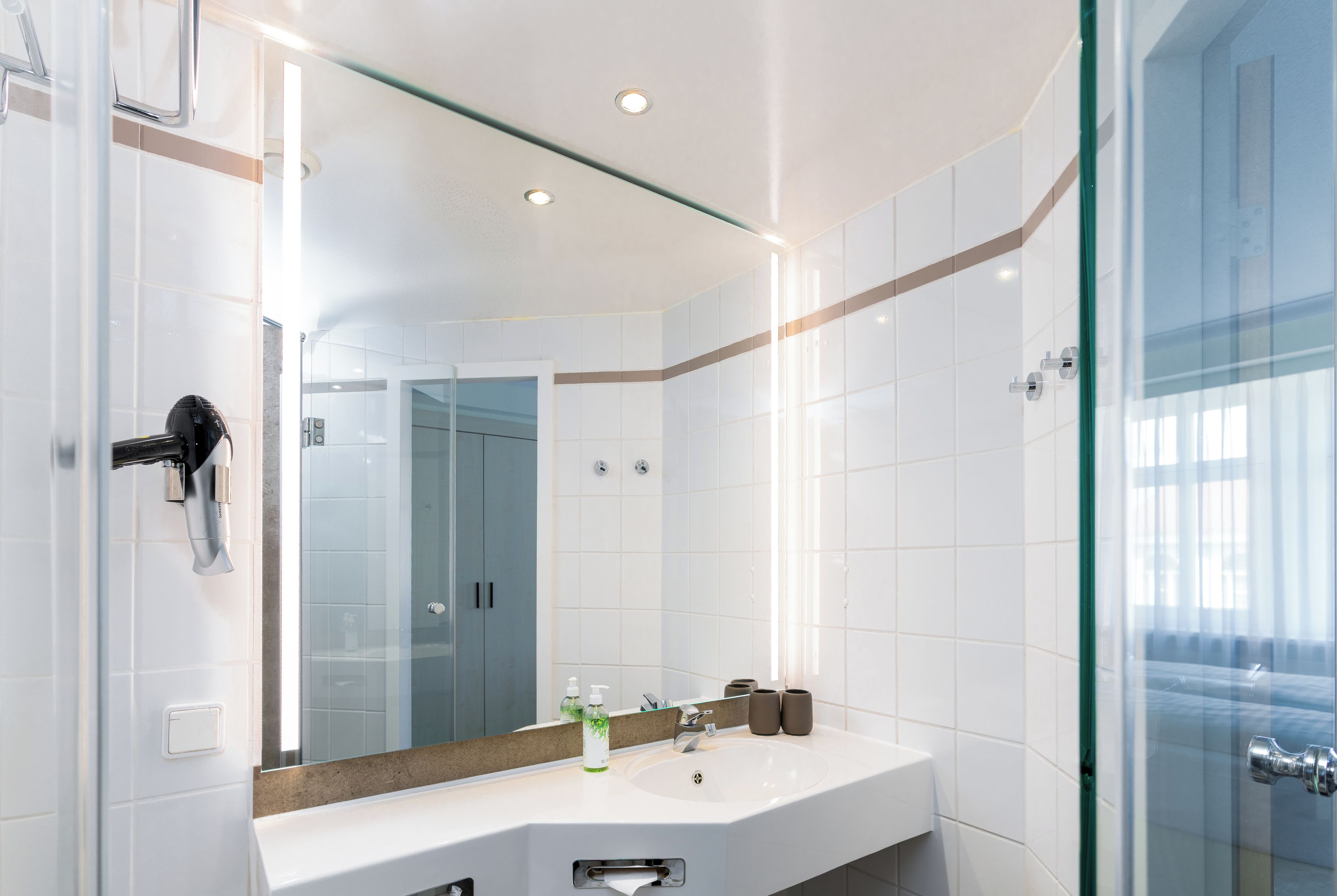 Ein modernes Badezimmer mit Duschkabine aus Glas, einem weißen Waschbecken mit Spiegel darüber und einem Handtuchhalter.