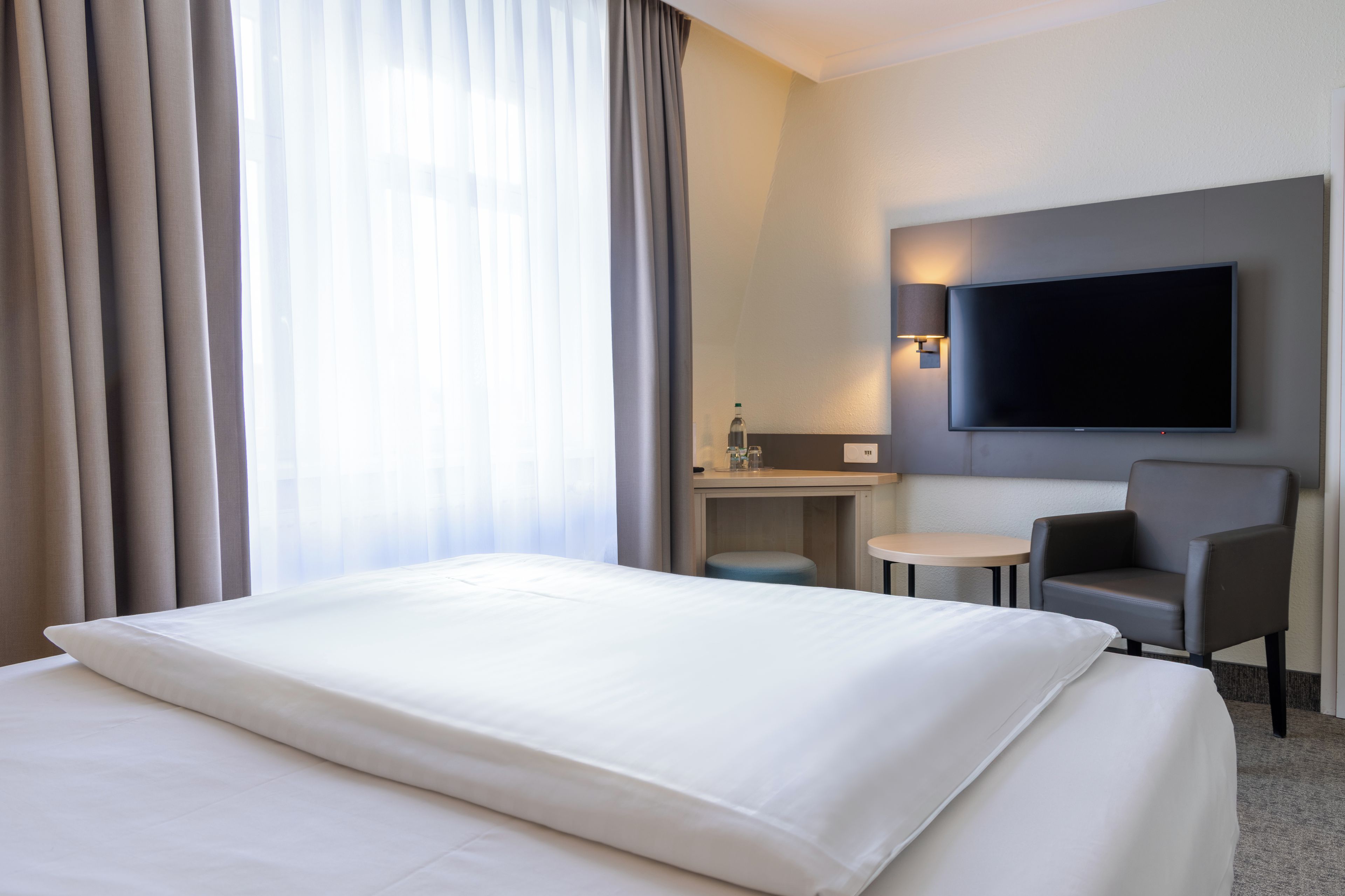 A hotel room with a bed, a TV mounted on the wall, a small table, and a chair.