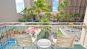 A balcony with two white chairs and a small round table, overlooking a street with palm trees and tall buildings.