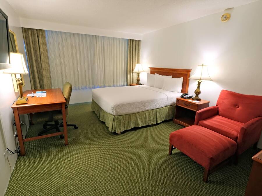 A hotel room with a bed, desk, chair, and two bedside lamps.