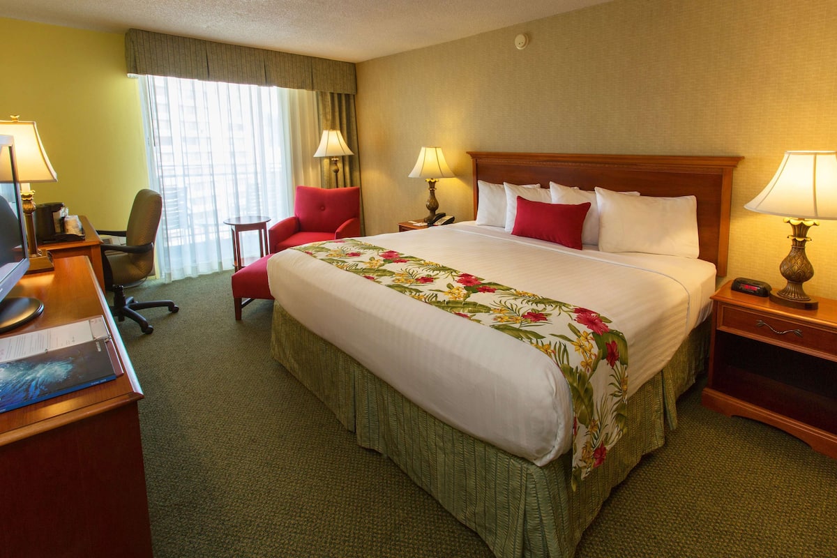 Een hotelkamer met een groot bed, een bureau met een computer, een stoel en twee bedlampen.