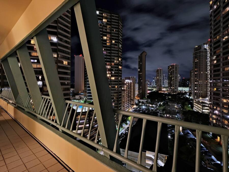 A nighttime cityscape with high-rise buildings, a bridge with green railings, and a tiled floor.
