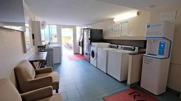 A hotel room with a bed, a desk, a chair, a washing machine, a dryer, and a water dispenser.