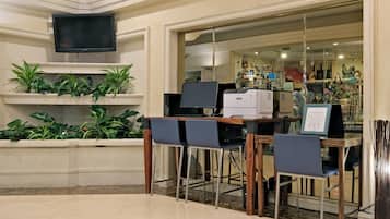 Un área de recepción con un televisor de pantalla plana, una computadora e impresora sobre un escritorio. Hay dos sillas y una planta a la izquierda.