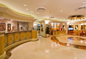 Un hall de hotel con mostrador de recepción, zona de estar y una planta grande.