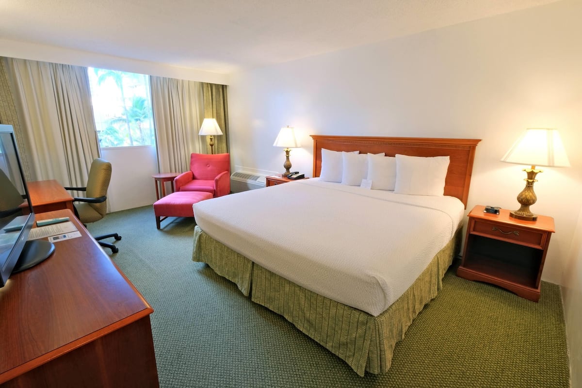 Hotelkamer met een bed, bureau met een computer, stoel, twee bedlampen en een raam met gordijnen.