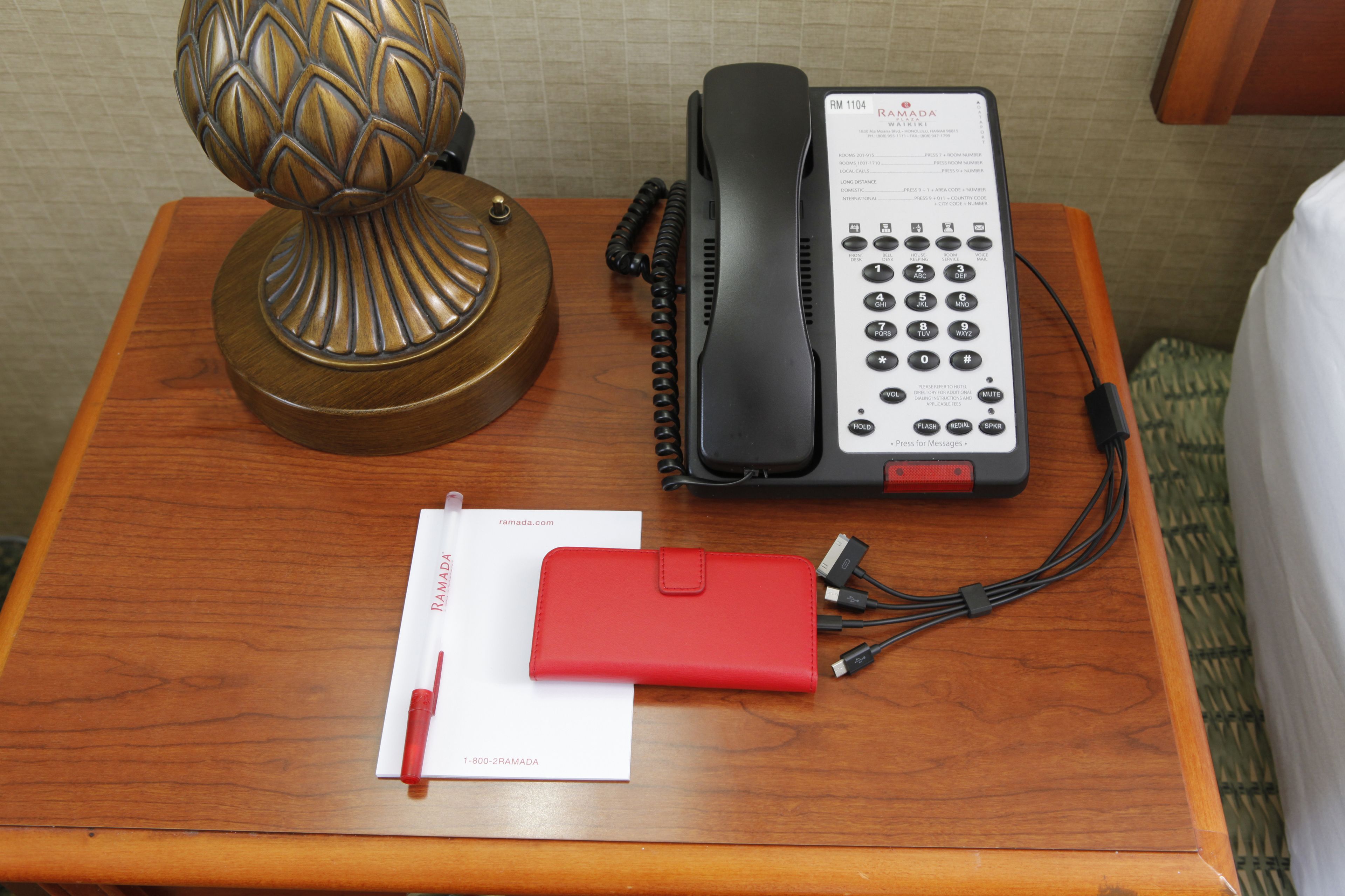 Ein Nachttisch aus Holz mit einem Festnetztelefon, einer roten Leder-Telefonablage, einem Stift und einer Visitenkarte.