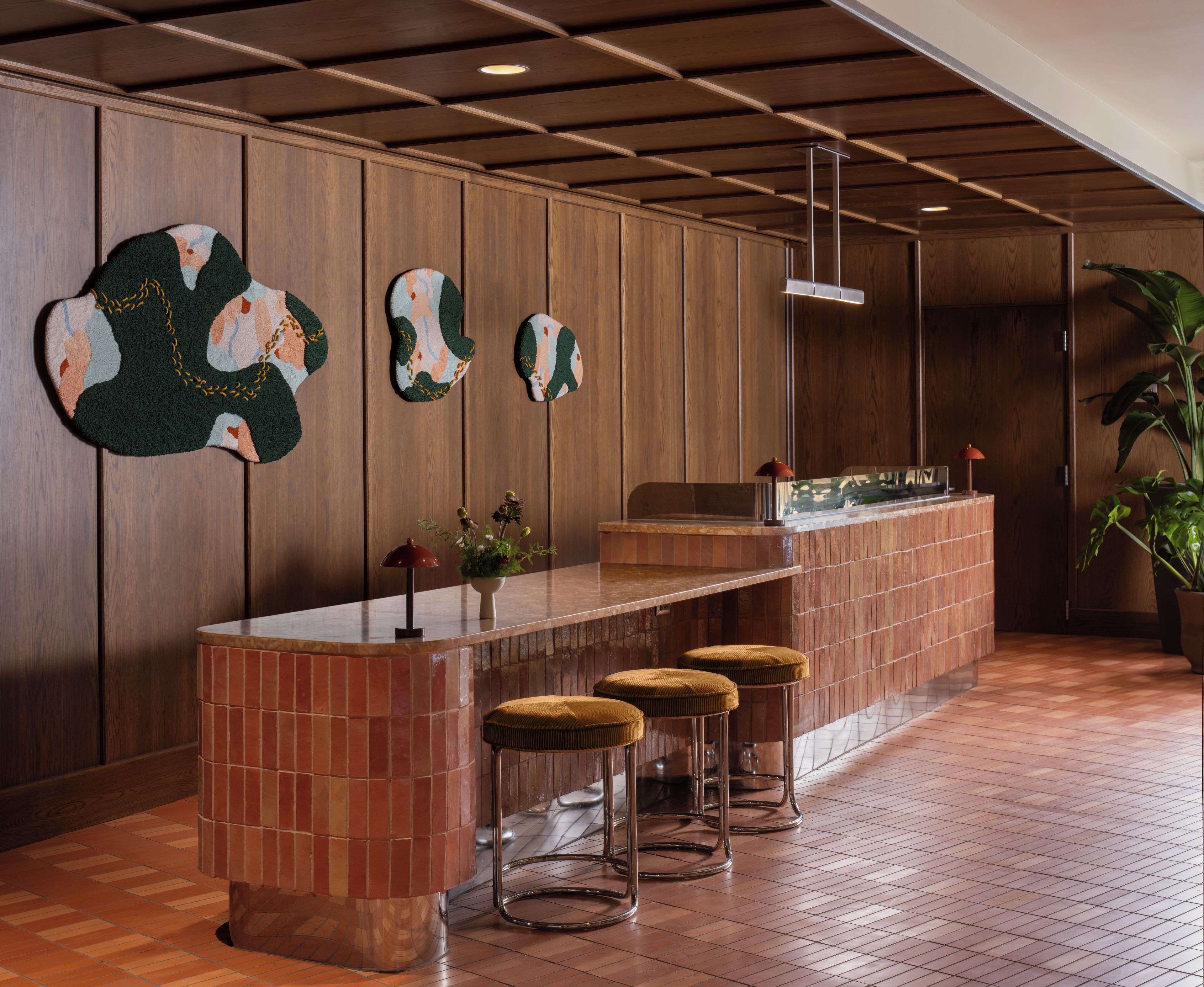 Una zona de bar con mostrador de madera, taburetes y una planta en maceta.