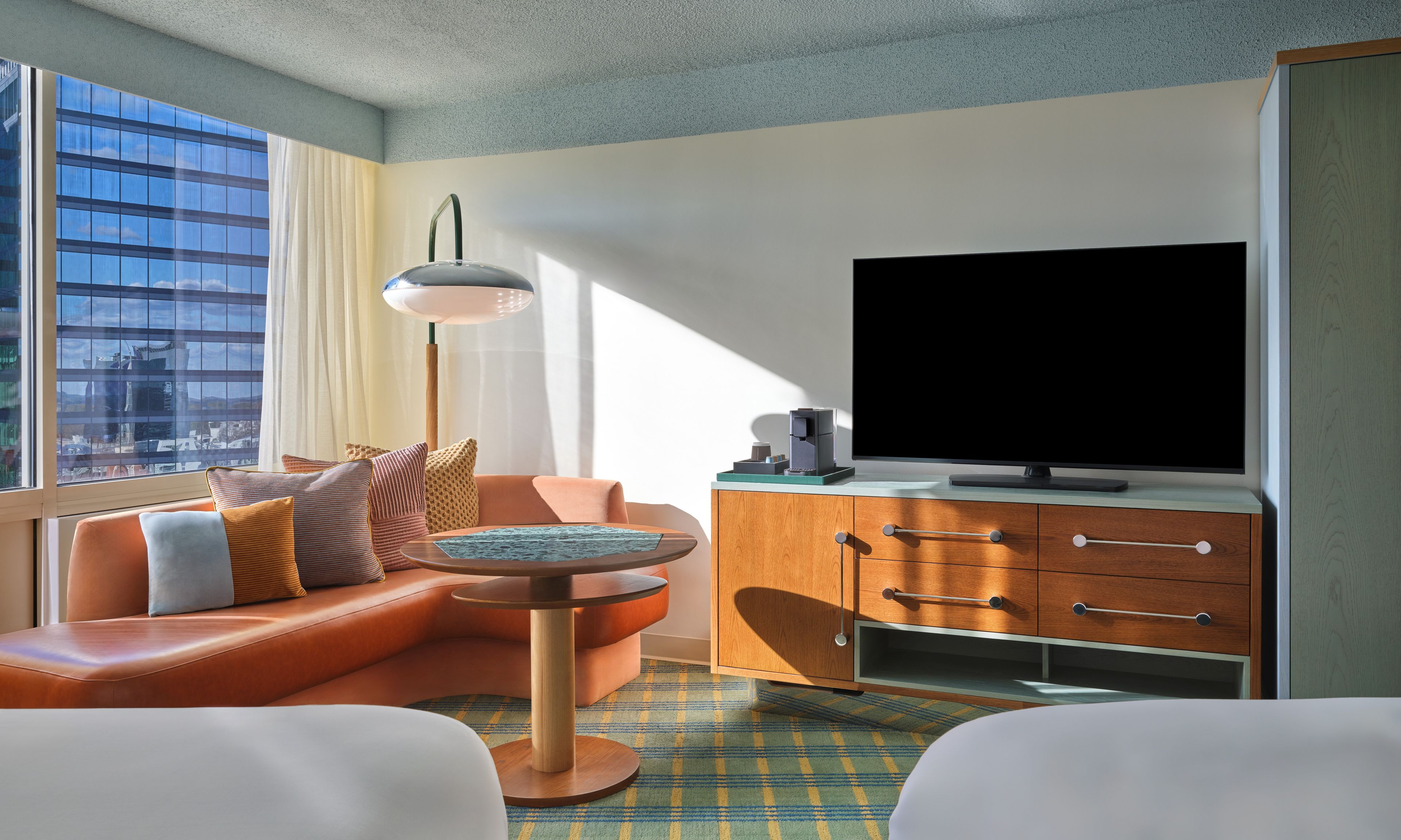 A modern hotel room with a leather sofa, a small round table, a television, and a cabinet.