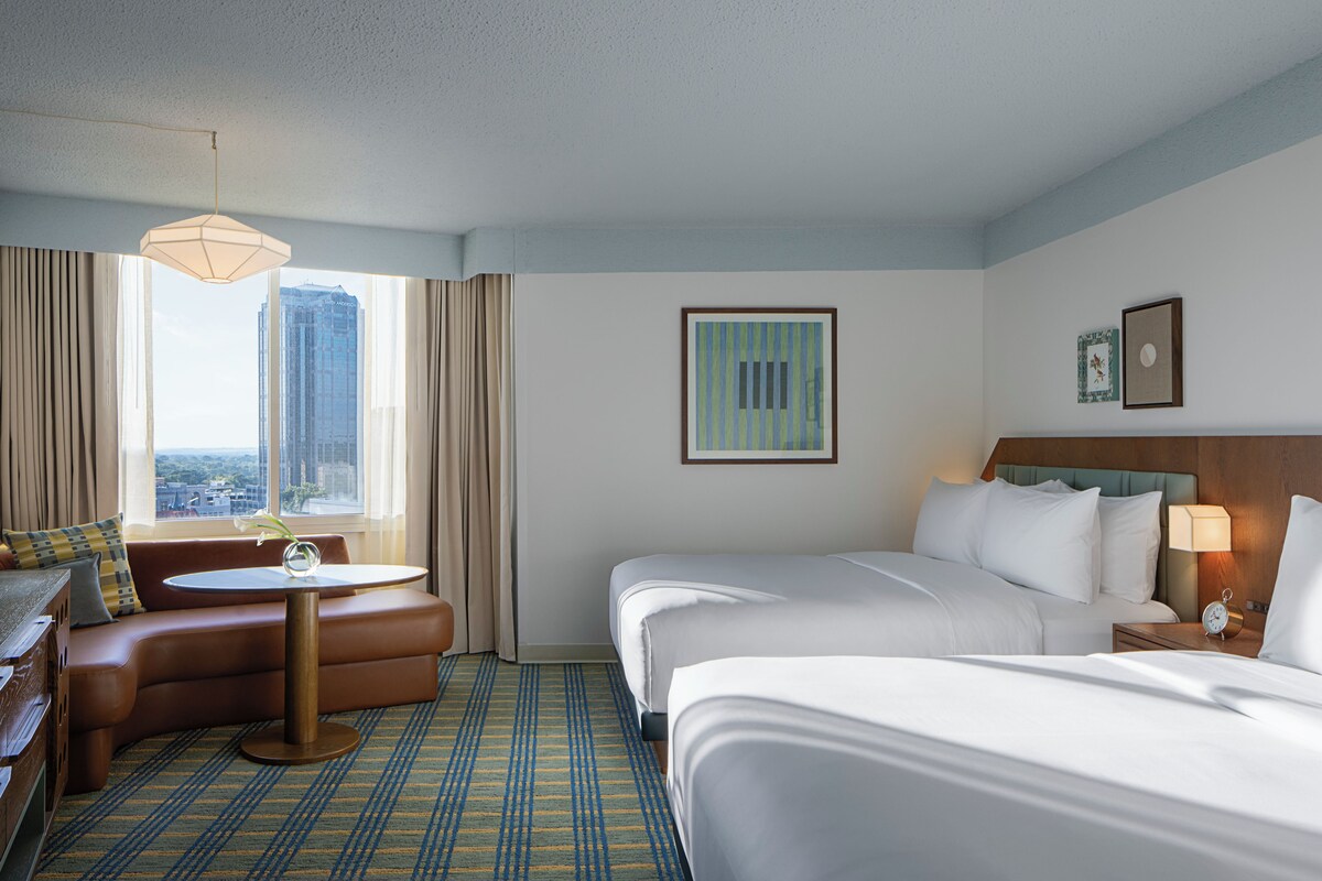 Habitación de hotel con cama, sofá, una mesita, lámpara y vistas a un paisaje urbano.