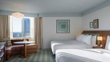 A hotel room with a bed, a sofa, a small table, a lamp, and a view of a cityscape.