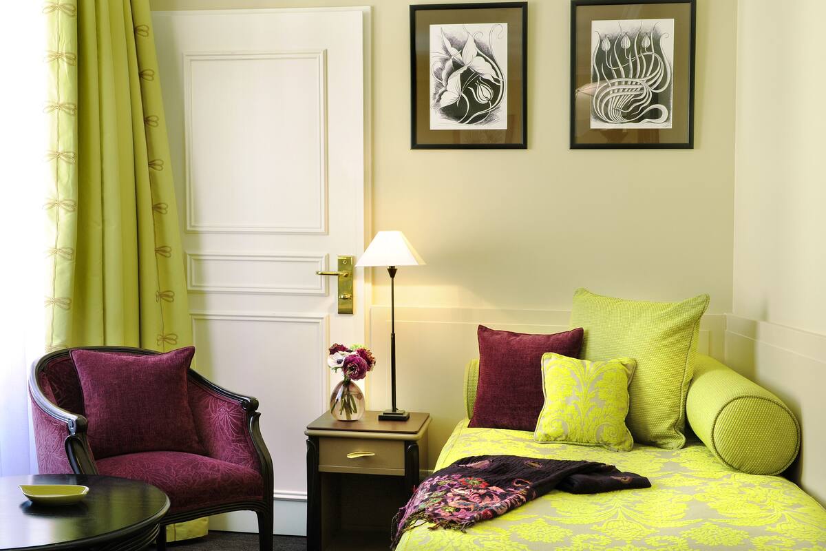 A room with a bed, a chair, a nightstand, a lamp, and two framed artworks on the wall.