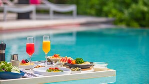 A poolside dining setup with a tray of food and drinks, including a salad, a fruit bowl, and two glasses of beverages. - InterContinental Bahrain by IHG (Manama)