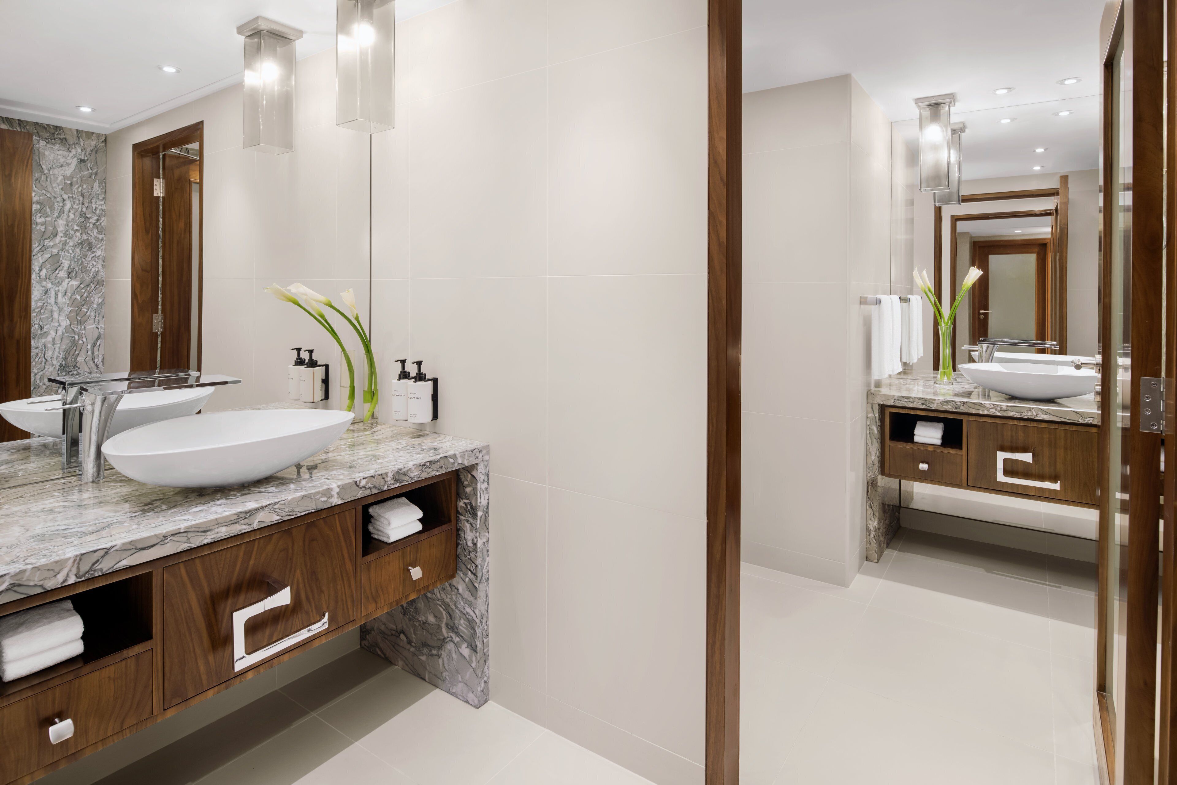 A modern bathroom with a large mirror, two sinks, marble countertops, wooden cabinets, and a marble backsplash.