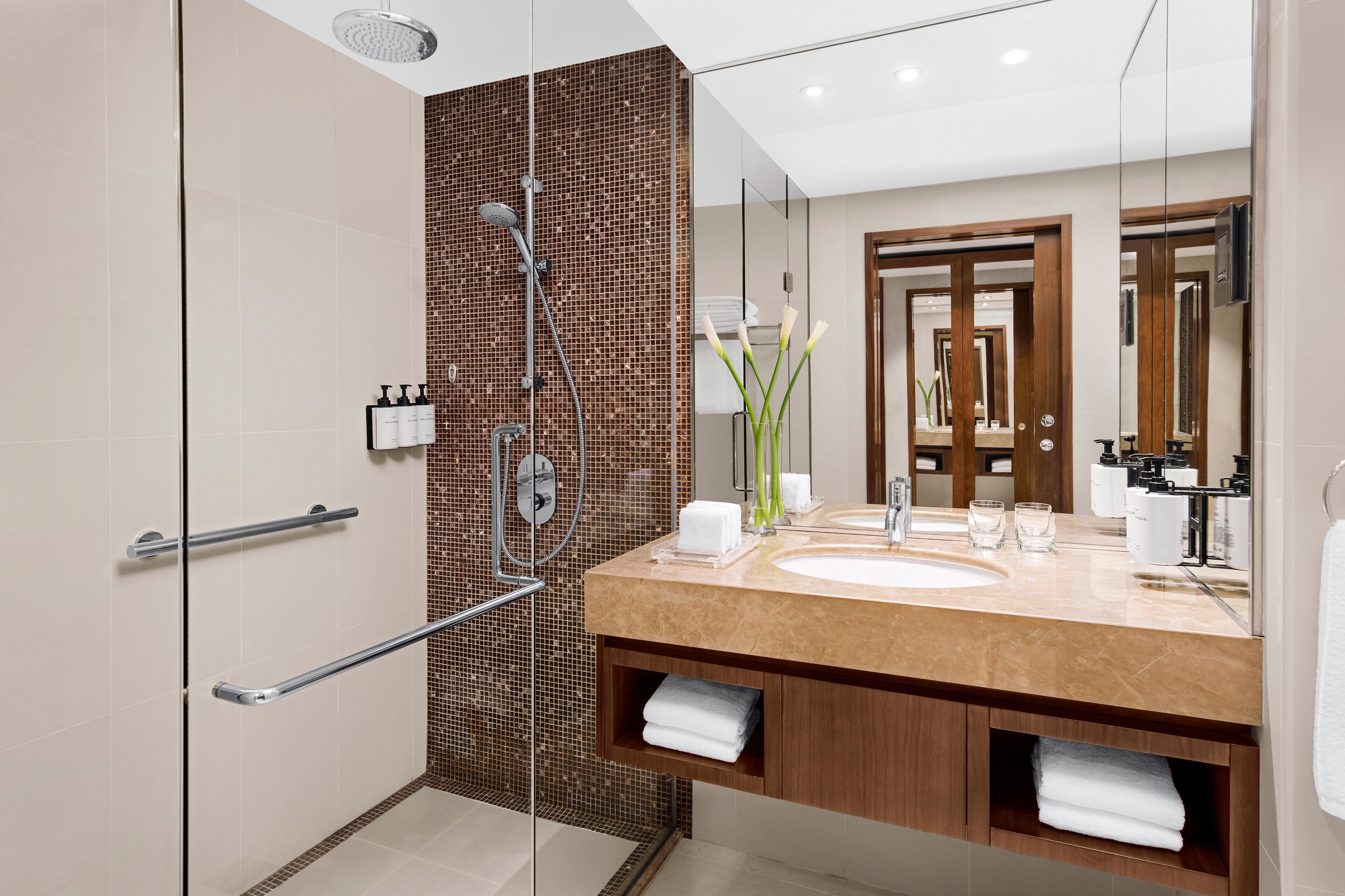 Een moderne badkamer met een douchecabine van glas, een groot wastafelmeubel met spiegel en houten kastjes.