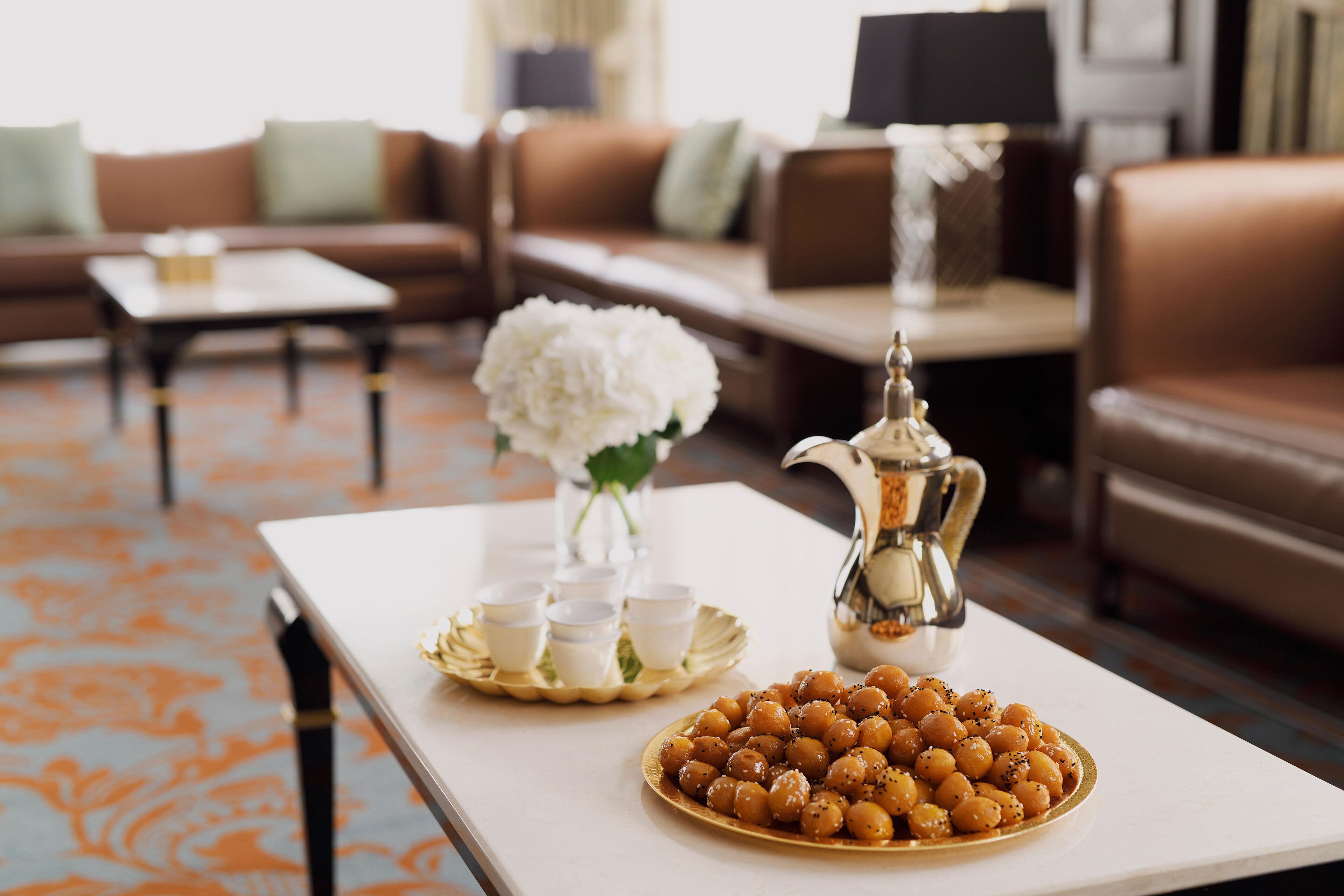 A living room with a white coffee table, a tray of white cups, a plate of sweets, and a silver pitcher.