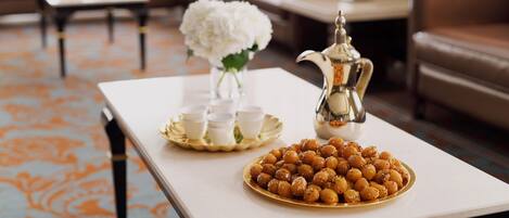 A living room with a white coffee table, a tray of white cups, a plate of sweets, and a silver pitcher.