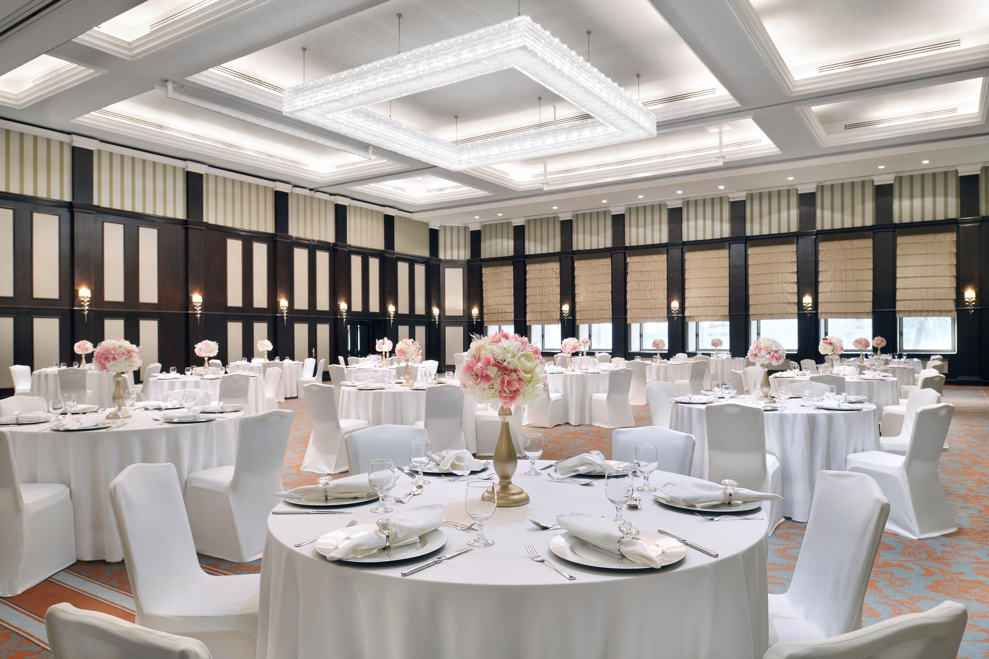 A large banquet hall with round tables set for a formal event, featuring white tablecloths, chairs, and floral centerpieces.