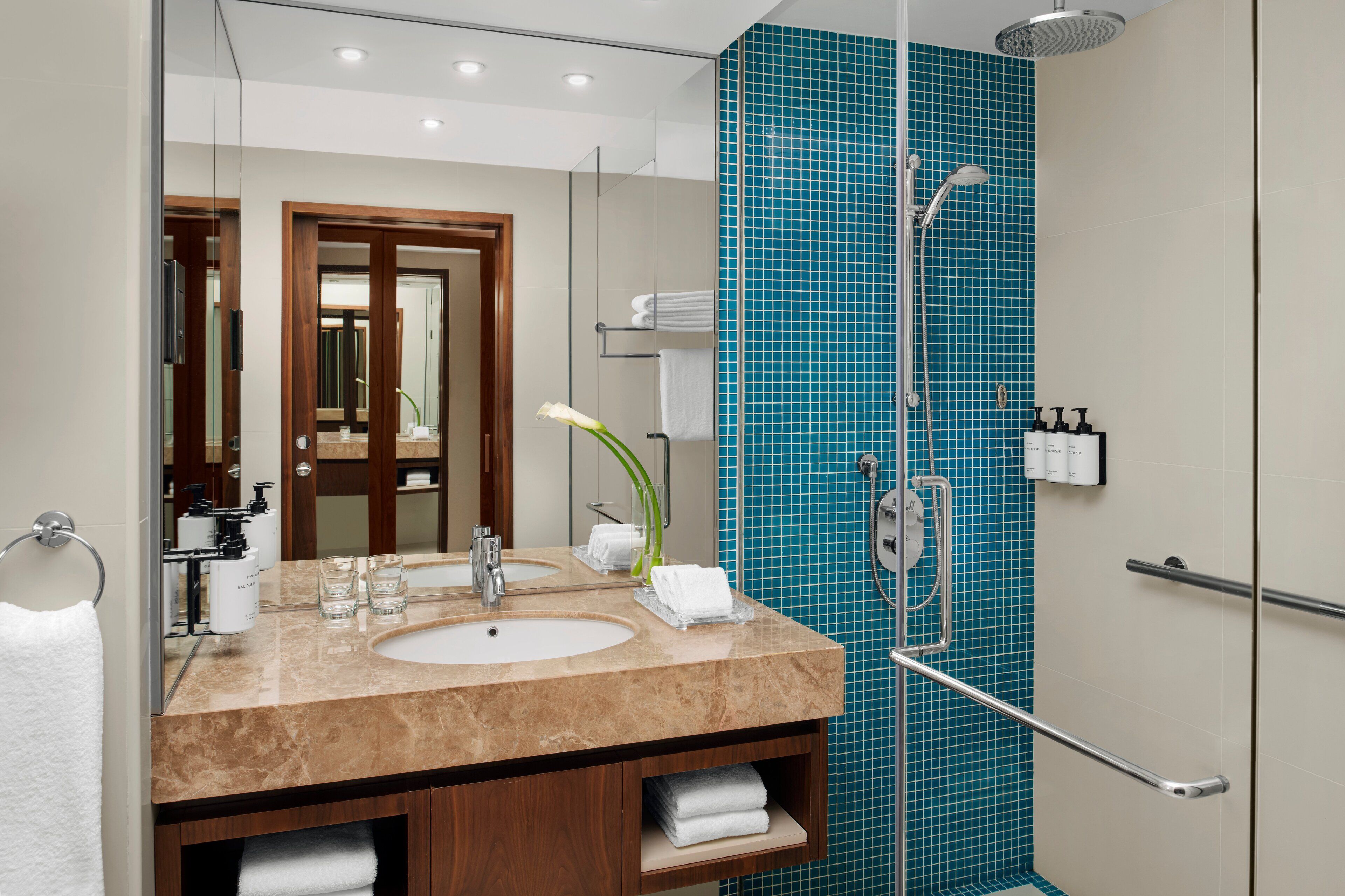 A modern bathroom with a marble sink, two mirrors, a glass shower enclosure, and a blue-tiled shower wall.