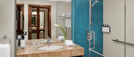 A modern bathroom with a marble sink, two mirrors, a glass shower enclosure, and a blue-tiled shower wall.