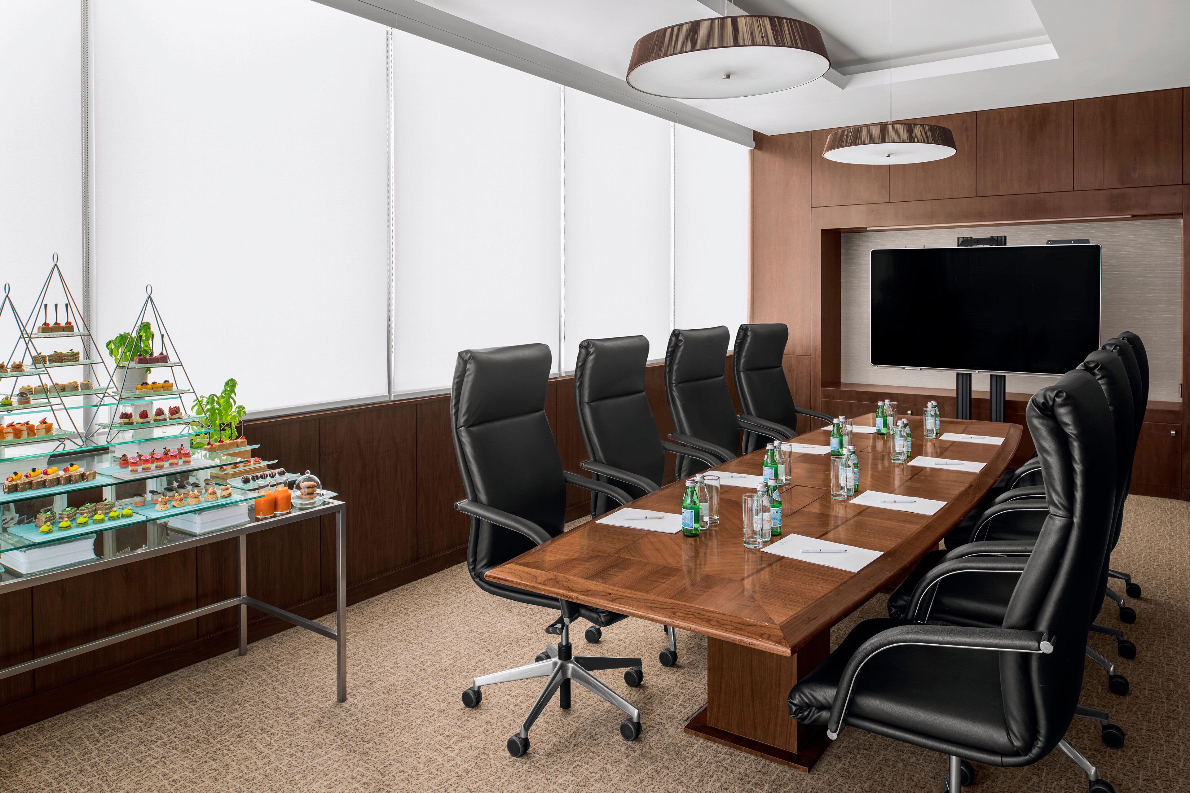A conference room with a long table, black chairs, a TV, and a display of food on the left.