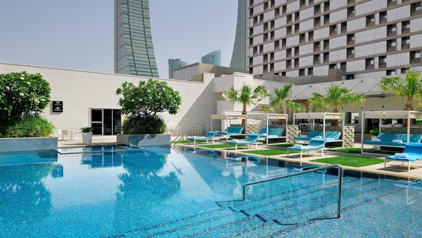 A swimming pool with lounge chairs and palm trees, surrounded by modern buildings. - InterContinental Bahrain by IHG (Manama)