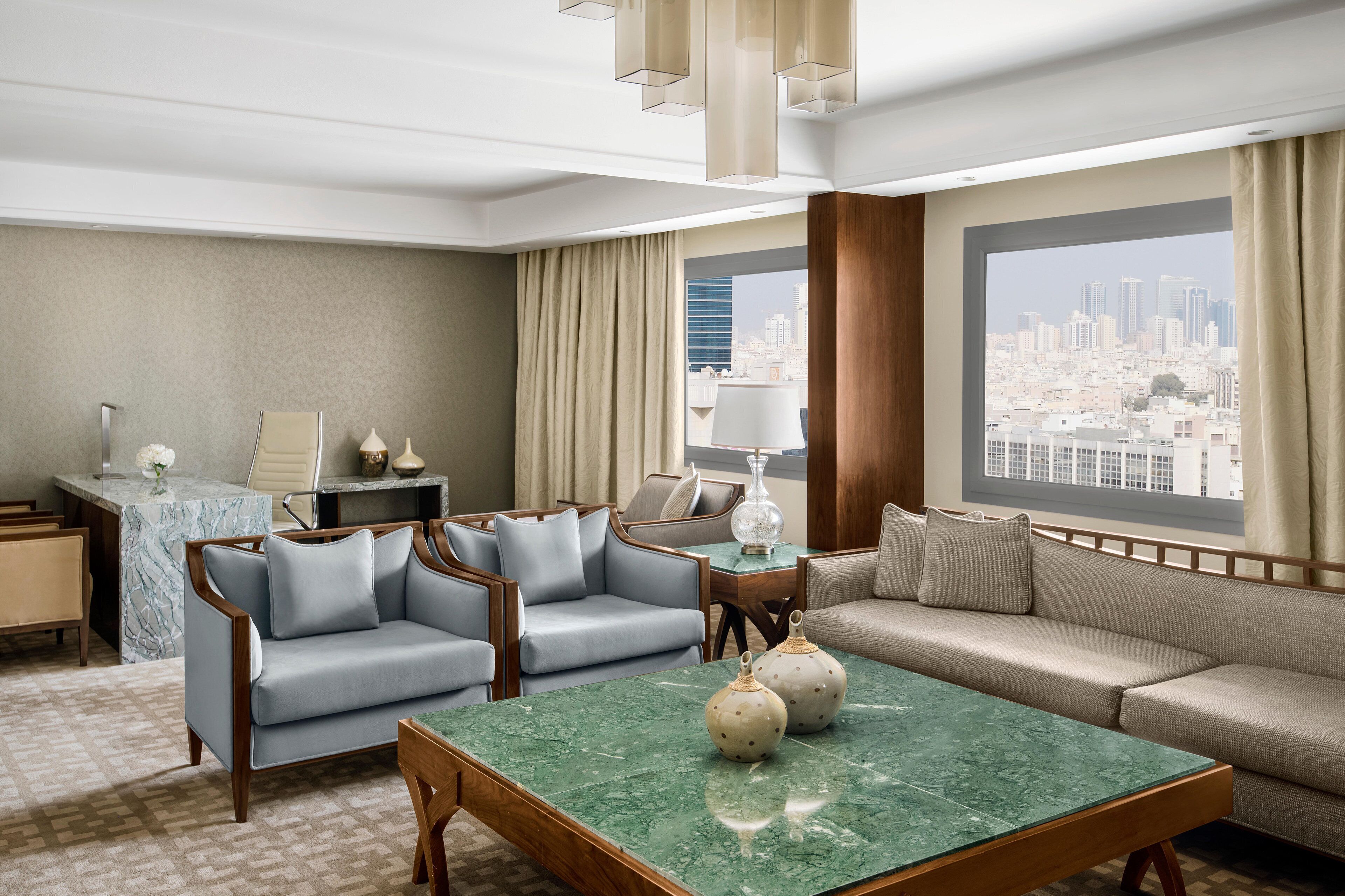 Ein modernes Hotelzimmer mit Blick auf die Stadt, einem мраморном журнальном столике und einer Sitzecke mit Sofas und Sesseln.