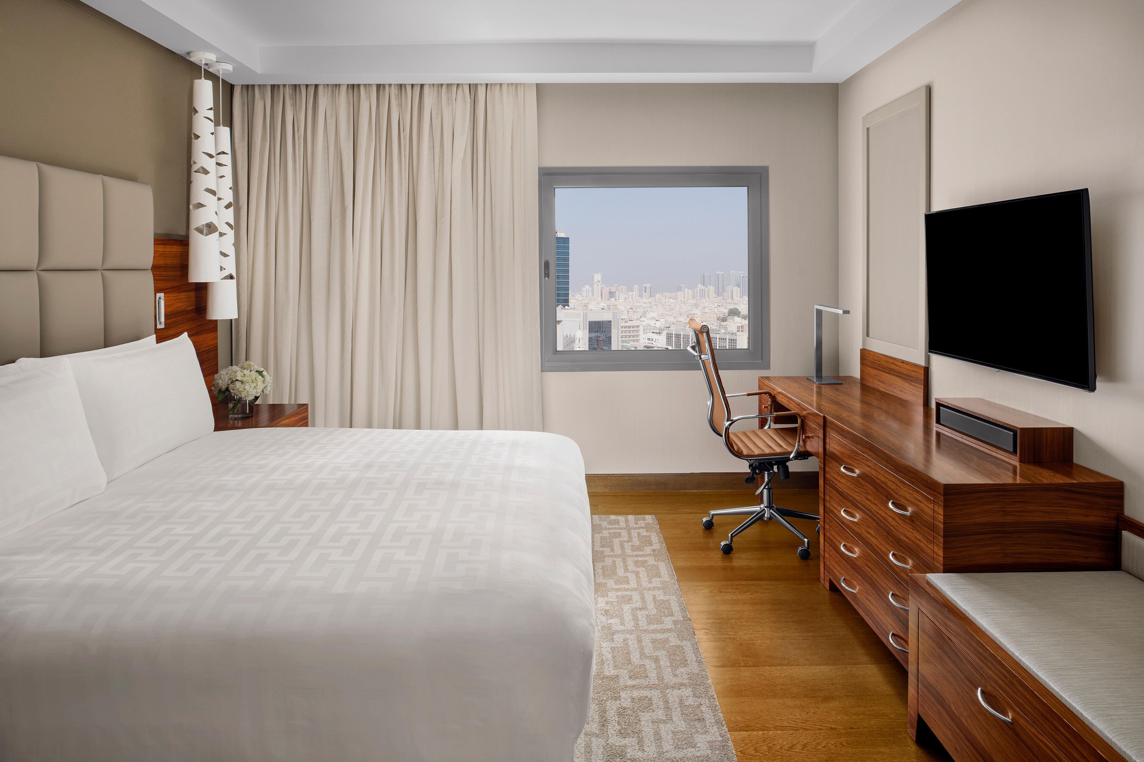 Una habitación de hotel con una cama grande, un escritorio con silla, televisión y ventana con vista a la ciudad.