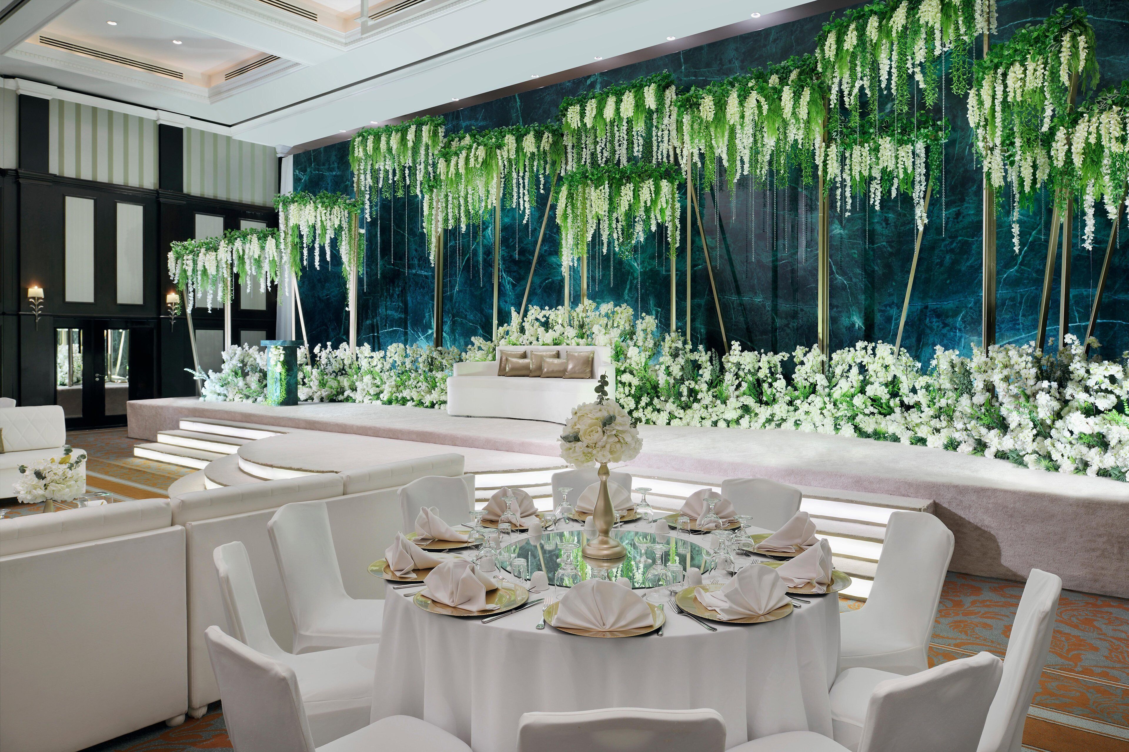 A formal dining area with round tables set for a meal, surrounded by white chairs.