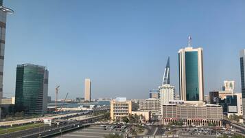A cityscape with modern high-rise buildings, a prominent tower with a flag, and a busy intersection with vehicles and a parking lot.