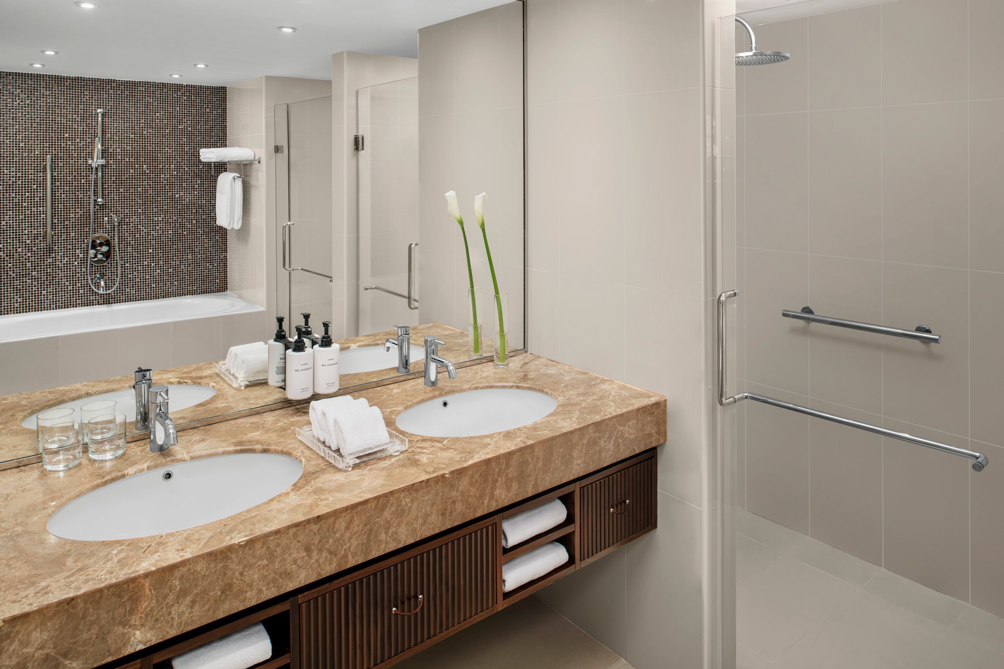 Un baño moderno con dos lavamanos, una ducha y zona de ducha con mampara de vidrio.