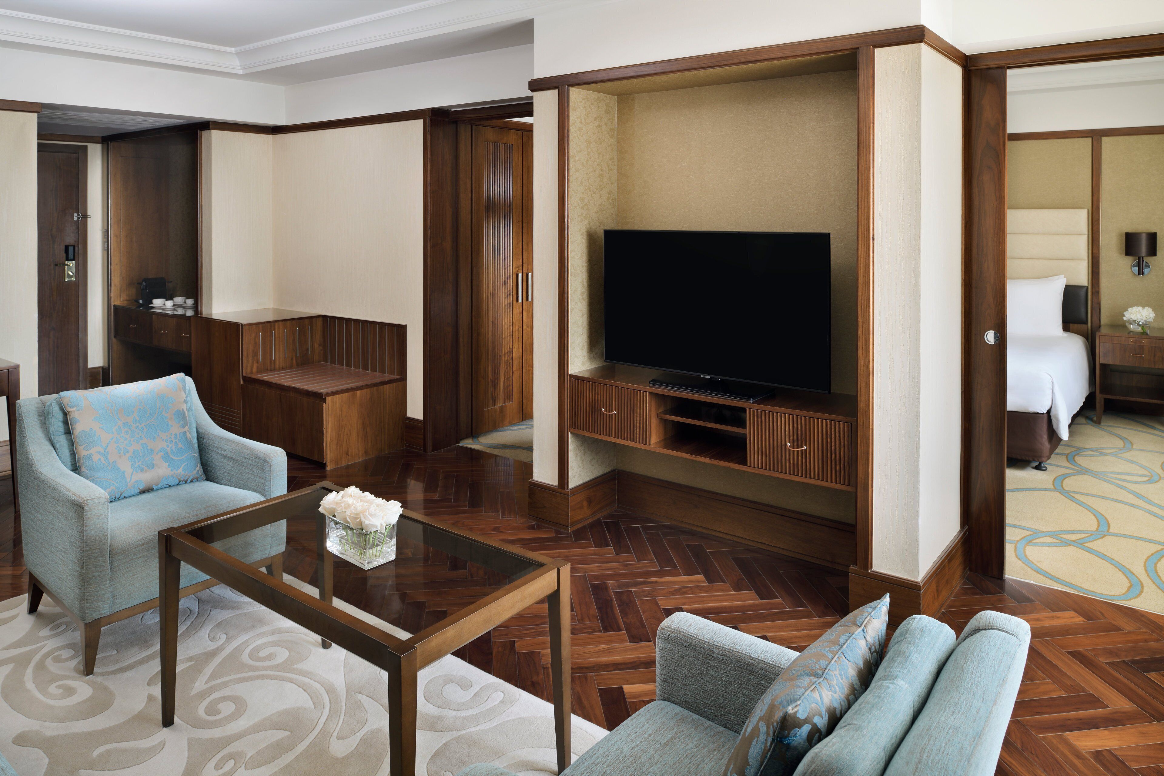 A hotel room with a television, seating area, and wooden flooring.