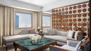 A modern hotel room with a large sofa, a coffee table, and a city view through large windows. - InterContinental Bahrain by IHG (Manama)